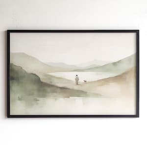 May include: A framed watercolor print depicting a serene landscape with muted green and beige tones. A figure in a robe walks with a small dog towards a body of water, with rolling hills and mountains in the background. The frame is black.