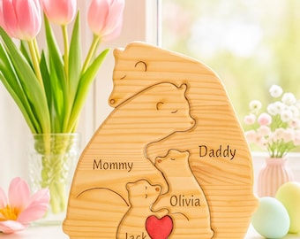 May include: Wooden family bear puzzle with the words "Mommy," "Daddy," "Olivia," and "Jack" engraved. A red heart is in the center. The bear puzzle is made of light-colored wood and is a decorative item.