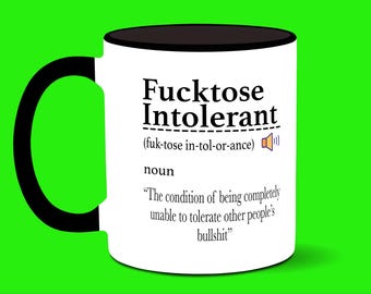 May include: White ceramic mug with a black handle and rim. The mug features the text "Fucktose Intolerant" in bold black letters, along with a definition. The background is bright green.