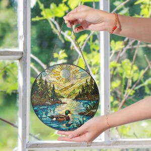 a hand holding a stained glass picture of a lake