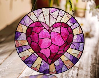 May include: A stained glass window hanging with a pink heart design. The heart is made of many small pieces of glass in shades of pink and purple. The background is a mix of yellow, purple, and white.