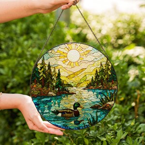 a hand holding a stained glass picture of a lake