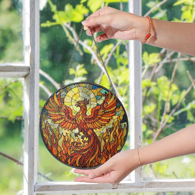 a hand holding a stained glass bird hanging from a window