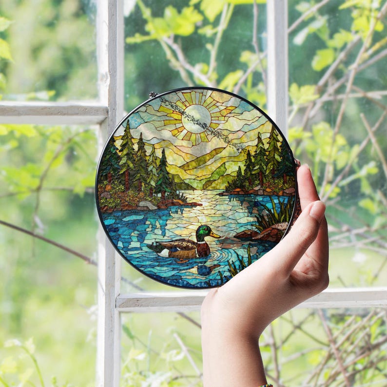 a hand holding a stained glass picture of a lake