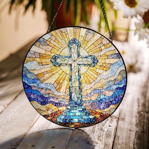 May include: A round stained glass window featuring a blue cross with a sunburst behind it. The cross is set against a background of blue and yellow stained glass.