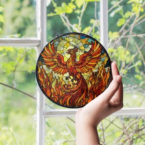 a hand holding a stained glass bird in front of a window