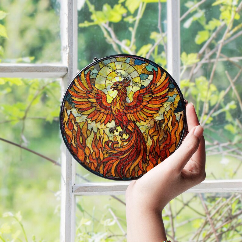 a hand holding a stained glass bird in front of a window