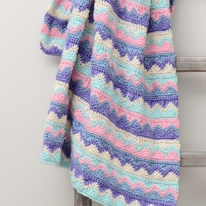 May include: A crocheted baby blanket with a chevron pattern in shades of purple, pink, blue, and cream.