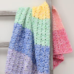 May include: A handmade crochet blanket in pastel colors, including lavender, blue, green, yellow, and pink. The blanket is draped over a wooden ladder, showcasing its textured stitch pattern and color gradient. This cozy blanket is perfect for home decor.