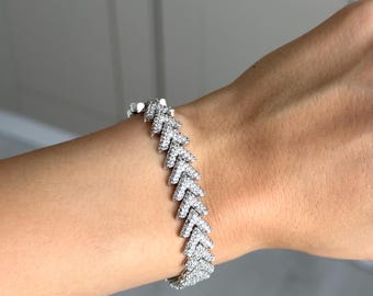 Op de afbeelding: Een zilveren armband met een herhalend chevron-ontwerp, bezet met kleine, heldere edelstenen. De armband wordt getoond op een pols, waarbij de glinsterende uitstraling wordt benadrukt. Dit sieraad is een modeaccessoire.