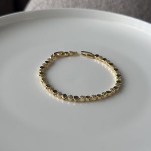 May include: A gold-coloured bracelet with a delicate design. The bracelet features small, round links, some adorned with sparkling accents. The bracelet is displayed on a white surface, showcasing its elegant simplicity. A classic piece of jewellery.