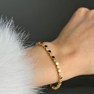 May include: Gold bracelet with circular links, some with small clear stones, others with dark accents. The bracelet is worn on a wrist. The background is dark. The bracelet is likely made of gold.