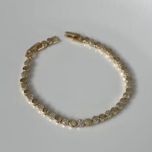 May include: A gold bracelet featuring a series of round, clear gemstones set in bezels. The bracelet is made of gold-toned metal and has a clasp. The gemstones are evenly spaced along the bracelet's length.