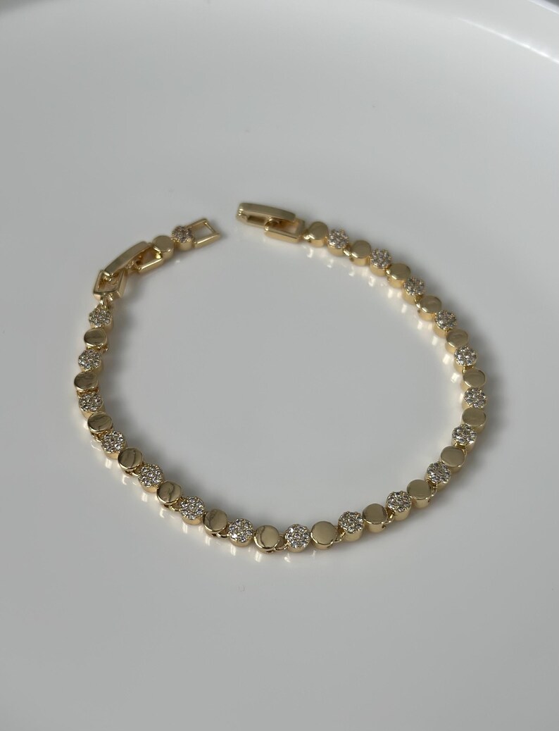 May include: A gold bracelet featuring a series of round, clear gemstones set in bezels. The bracelet is made of gold-toned metal and has a clasp. The gemstones are evenly spaced along the bracelet's length.