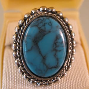 Puede incluir: Un anillo de plata con una gran piedra ovalada turquesa engastada en un diseño de cuerda.
