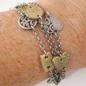 May include: A silver and gold charm bracelet with multiple chains and charms, including hearts, circles, and a swirl design.