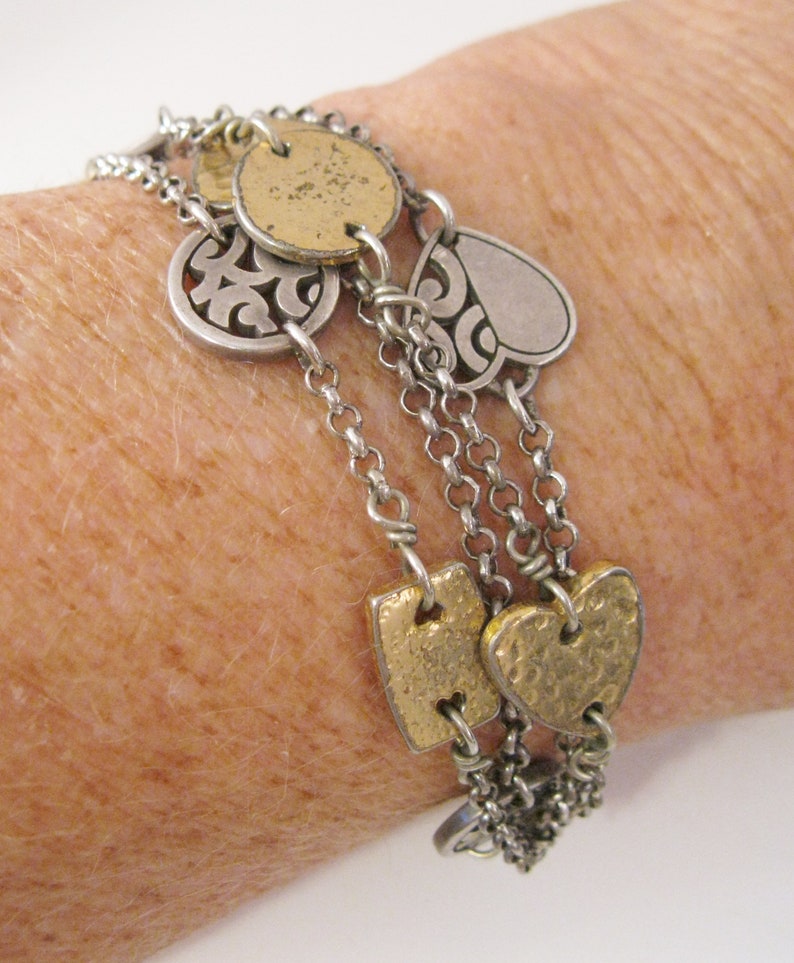 May include: A silver and gold charm bracelet with multiple chains and charms, including hearts, circles, and a swirl design.