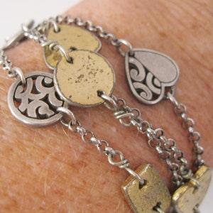 May include: A silver and gold chain bracelet with multiple charms, including a heart, circles, and a swirl design.
