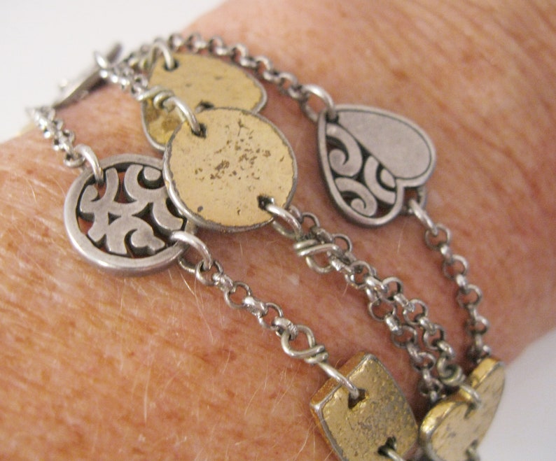 May include: A silver and gold chain bracelet with multiple charms, including a heart, circles, and a swirl design.