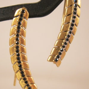 May include: A pair of gold earrings with black stones set in a feather design.