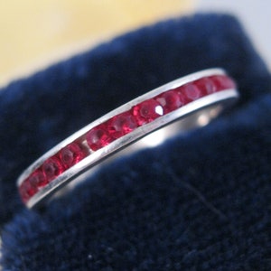 Puede incluir: Un anillo de banda de plata con una fila de piedras de rubí rojo.