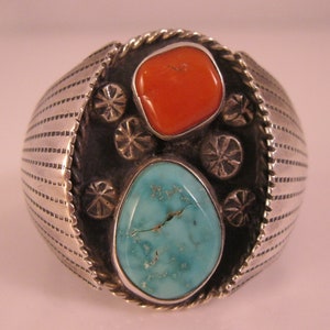 May include: A silver ring with a turquoise and coral inlay. The ring has a textured band and a design of small silver flowers around the stones.
