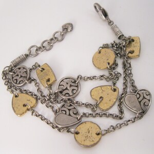 May include: A silver and gold multi-strand bracelet with heart and circle charms. The charms have a textured, hammered finish and some feature a swirling design.