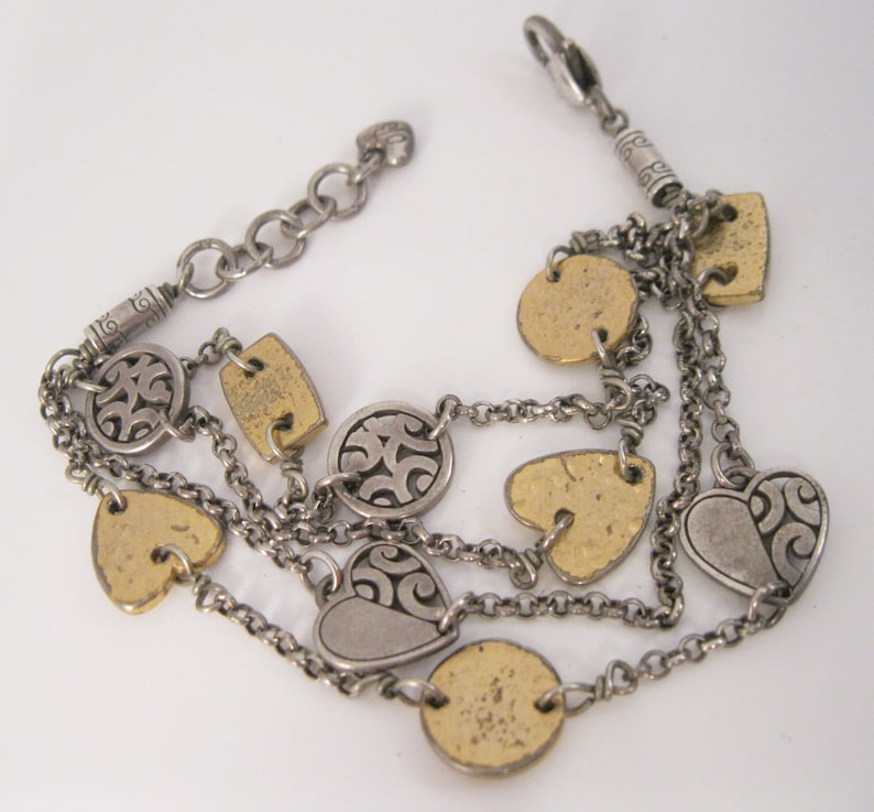 May include: A silver and gold multi-strand bracelet with heart and circle charms. The charms have a textured, hammered finish and some feature a swirling design.