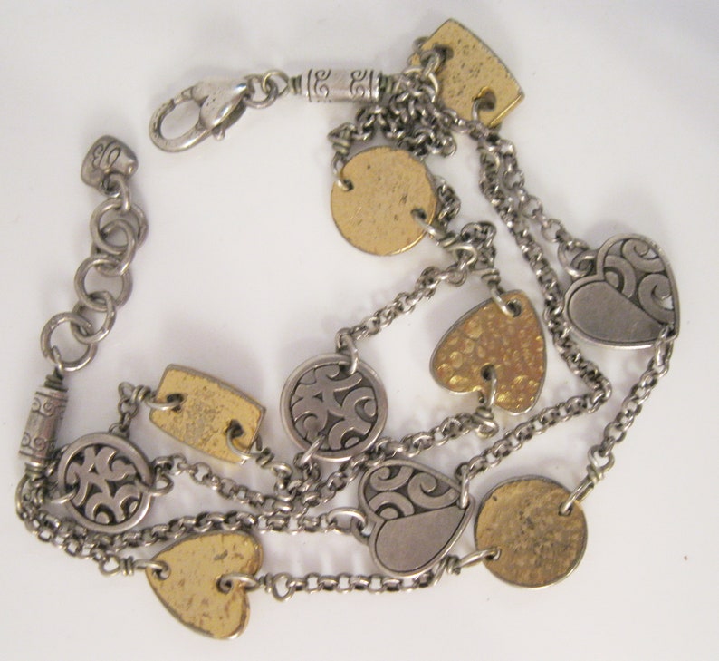 May include: A silver and gold multi-strand bracelet with a variety of charms, including hearts, circles, and squares.