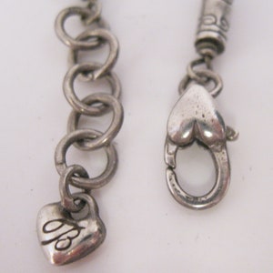 May include: Silver chain necklace with a heart-shaped clasp and a small heart charm with the letter "B" engraved on it.