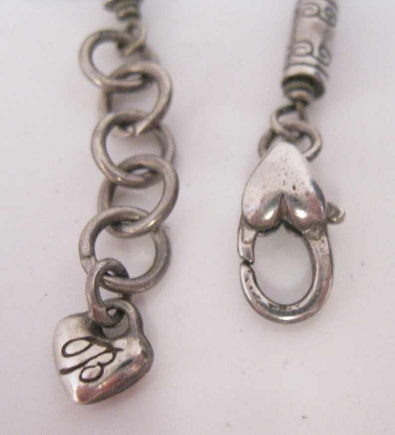 May include: Silver chain necklace with a heart-shaped clasp and a small heart charm with the letter "B" engraved on it.