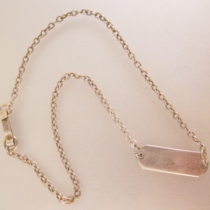 May include: A silver chain necklace with a rectangular tag pendant.