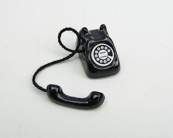 May include: A black rotary phone with a black cord and a black handset. The phone has a round dial with white numbers.