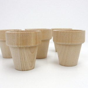 May include: Six unfinished wooden plant pots, each with a slightly different shape and size. The pots are made of light brown wood and have a natural, rustic look.