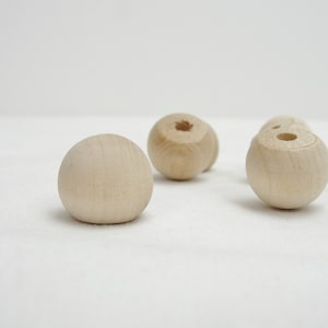 May include: A collection of unfinished wooden beads. The beads are spherical, with a natural wood color and visible grain. Some beads have a hole drilled through them, suggesting they are for stringing or crafting projects.