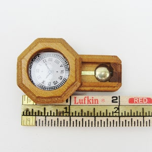 May include: A miniature wooden clock with a pendulum, measuring approximately 2 inches in length. The clock face has Roman numerals and a black hand.