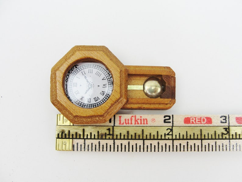 May include: A miniature wooden clock with a pendulum, measuring approximately 2 inches in length. The clock face has Roman numerals and a black hand.