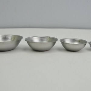 May include: Four silver metal bowls of varying sizes, arranged from largest to smallest.