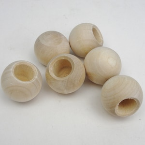 May include: Six unfinished wooden balls with a hole in the center. The balls are light brown and have a smooth surface.