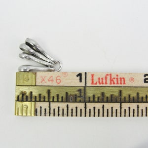 May include: Silver-toned metal pendant charm with a fan-like design. The charm is measured against a ruler, showing it is approximately 1 inch in length.
