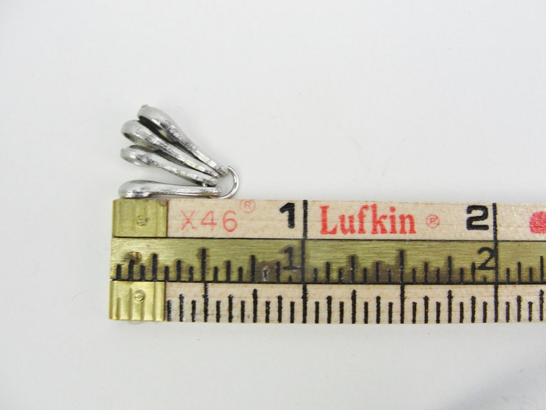May include: Silver-toned metal pendant charm with a fan-like design. The charm is measured against a ruler, showing it is approximately 1 inch in length.