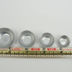 May include: Four silver metal bowls of varying sizes, lined up from largest to smallest, measured with a ruler. The ruler reads "Lufkin" and "RED END".
