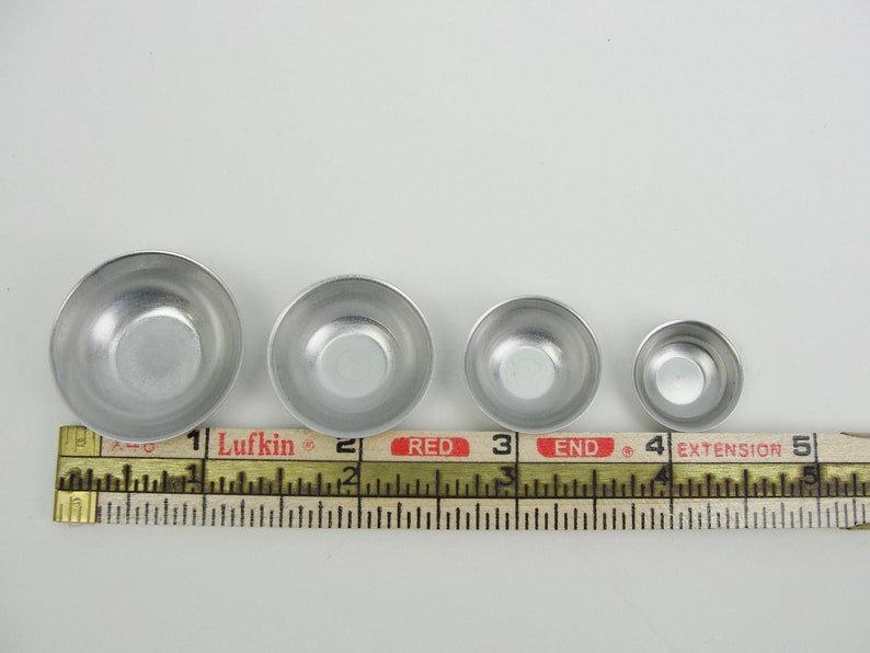 May include: Four silver metal bowls of varying sizes, lined up from largest to smallest, measured with a ruler. The ruler reads "Lufkin" and "RED END".
