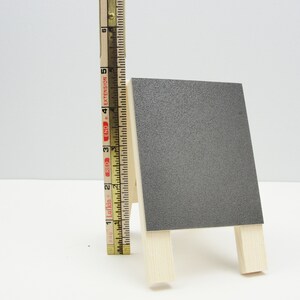 May include: A small, gray chalkboard easel with a wooden frame. The easel is about 6 inches tall.
