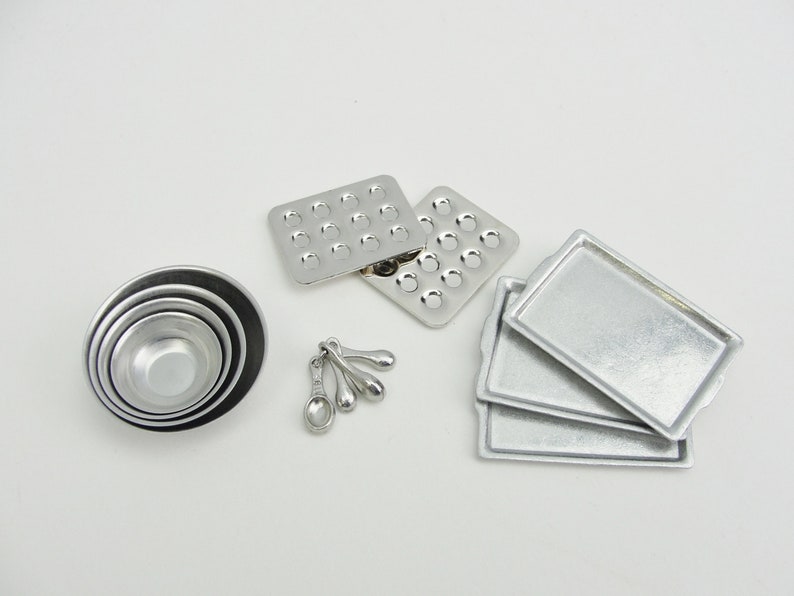 May include: A set of miniature silver baking tools, including four measuring spoons, a set of four nesting bowls, two muffin tins, and three baking sheets.
