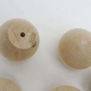 May include: A set of six unfinished wooden balls with a hole drilled through the center of each ball. The balls are smooth and have a natural wood color.