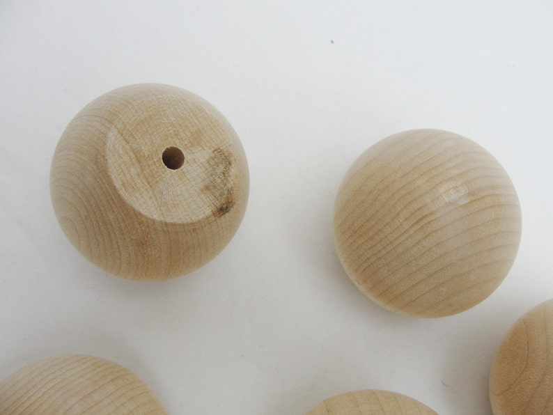 Puede incluir: Un conjunto de seis bolas de madera sin terminar con un agujero perforado en el centro de cada bola. Las bolas son lisas y tienen un color de madera natural.