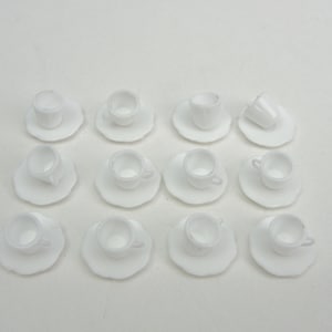 May include: A set of 12 white miniature teacups and saucers. The cups and saucers are made of a smooth, white ceramic material.
