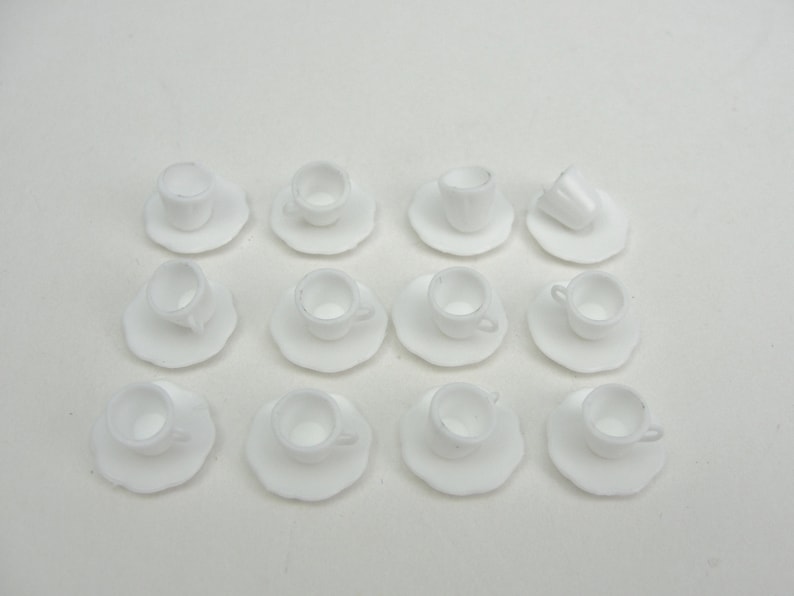 May include: A set of 12 white miniature teacups and saucers. The cups and saucers are made of a smooth, white ceramic material.