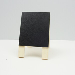 May include: A small black chalkboard easel with wooden legs. The chalkboard is blank and ready for writing.